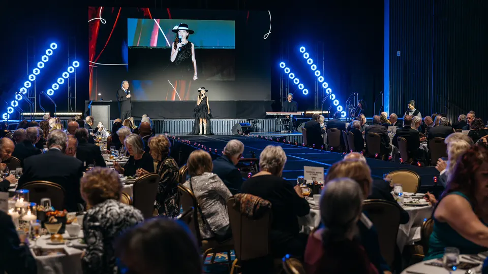Ballroom guests watching the Hope & Home fashion show under blue stage lights